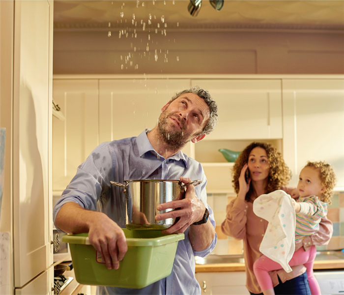 a man standing next to his family with buckets in hand to catch the water falling from their ceiling